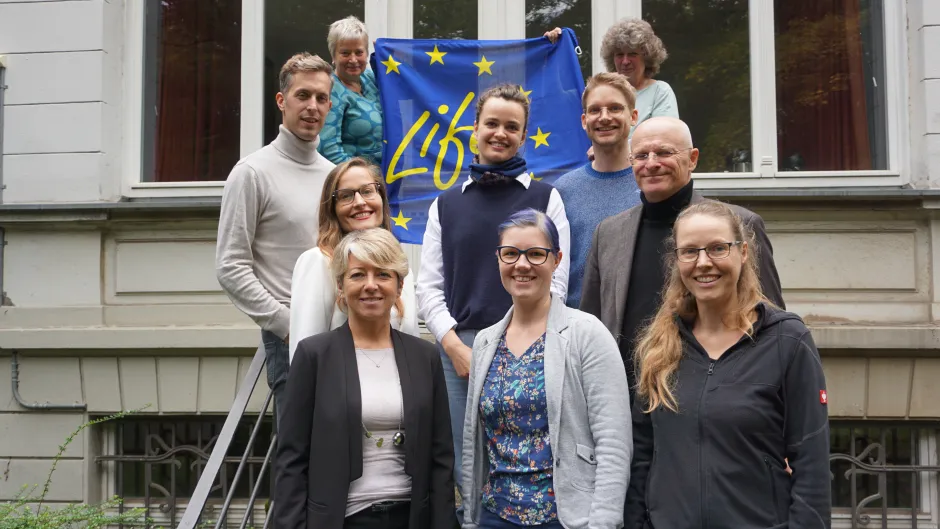 Gruppenfoto mit EU-blauer Flagge mit der Aufschrift "Life", außenherum gelbe Sterne